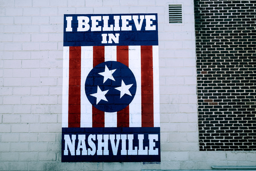 “I Believe in Nashville” sign painted on a white brick wall|Concrete urban building with green Tennessee sign