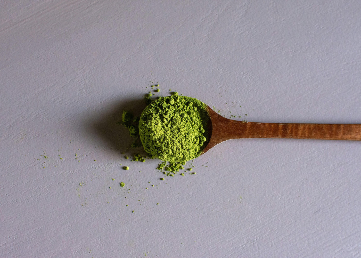 A Wooden Spoon Full of Green Kratom Powder Lying on a Pastel Table