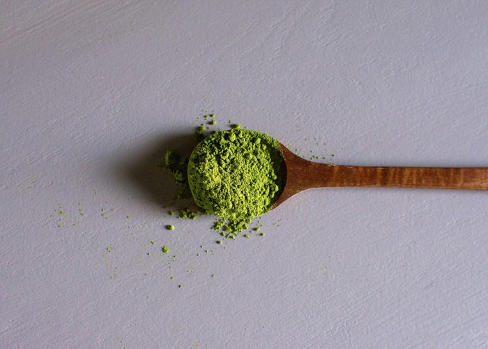 A Wooden Spoon Full of Green Kratom Powder Lying on a Pastel Table