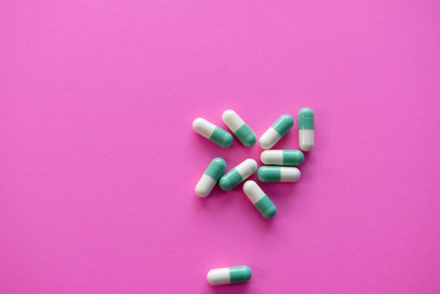 Green and white capsules on a pink background