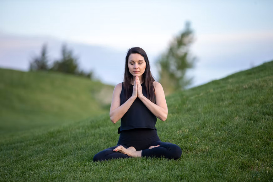 woman meditating on green grass field