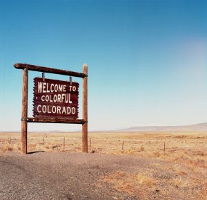 Wood sign in an open field reading “Welcome to Colorful Colorado”