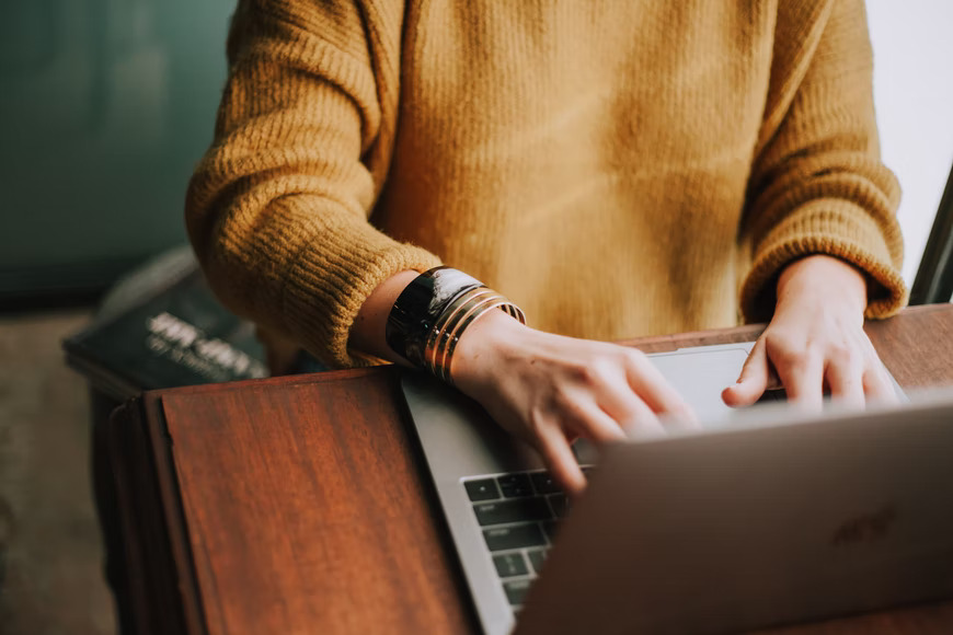 woman in sweater using laptop to buy kratom online