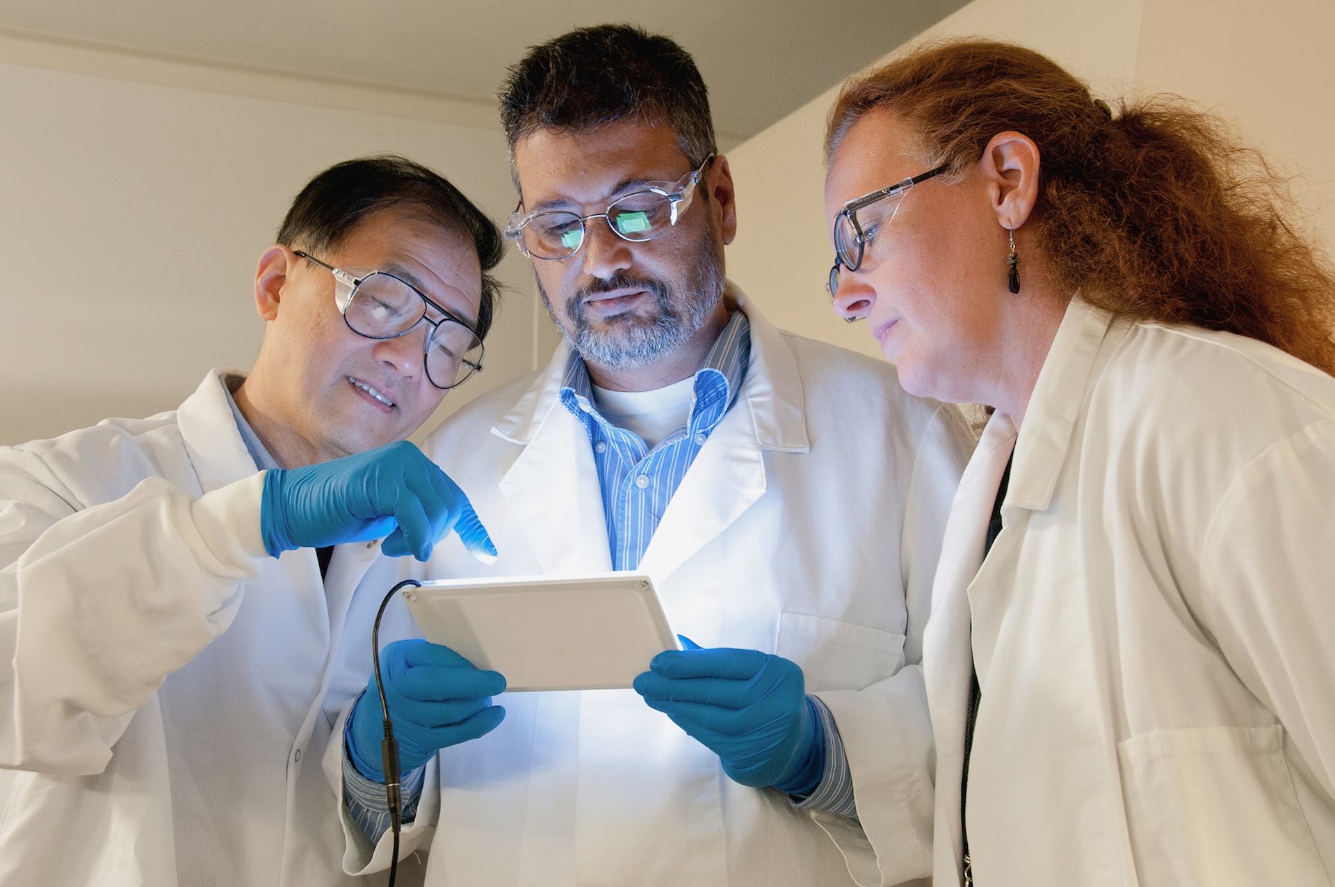 Three researchers in lab coats examining a tablet