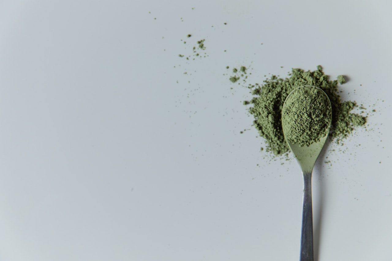 Spoon of green powder on white surface