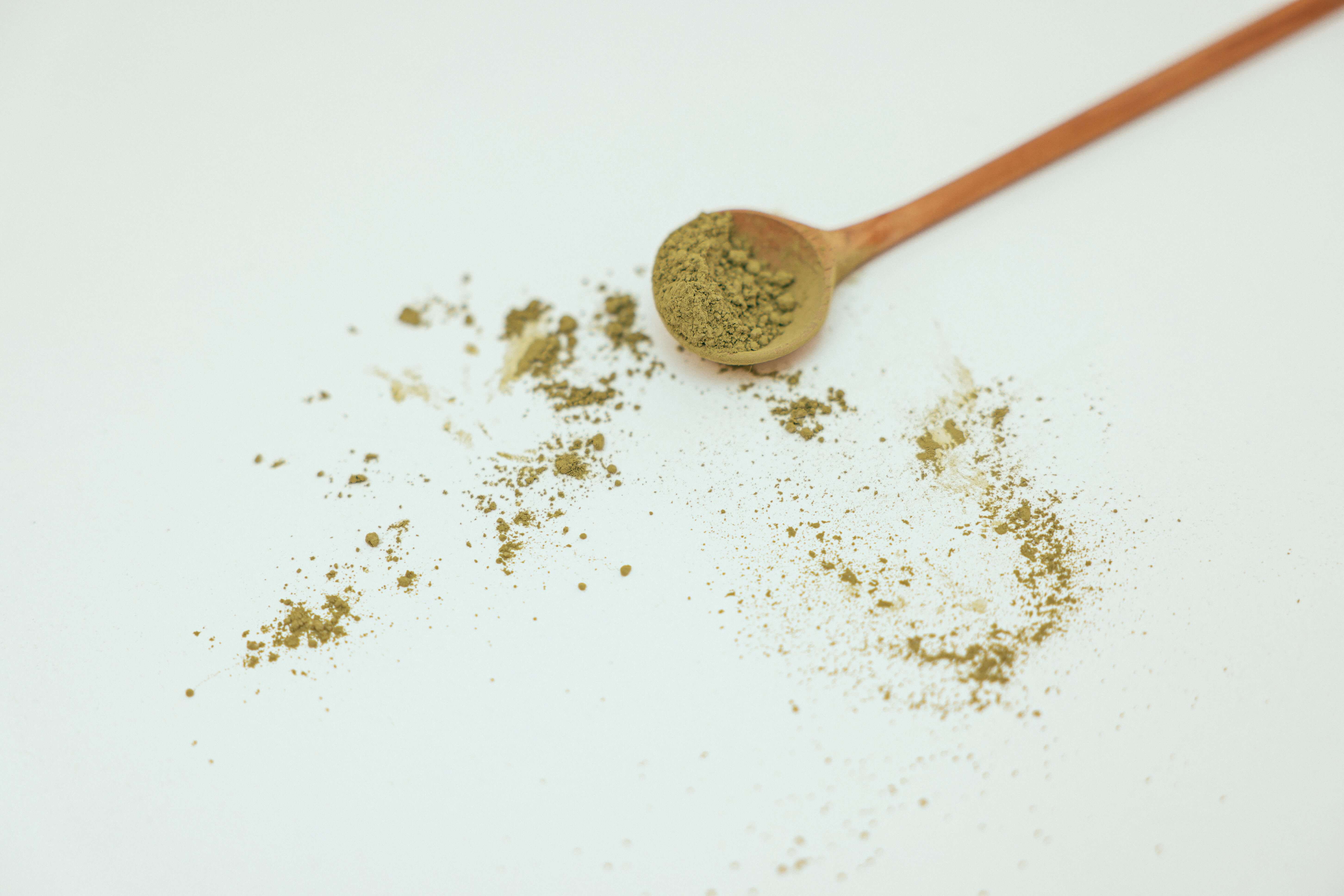 brown wooden spoon with kratom powder on white surface